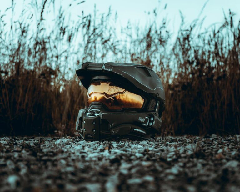A futuristic helmet with a reflective visor placed outdoors on rocky ground, bathed in sunset light.